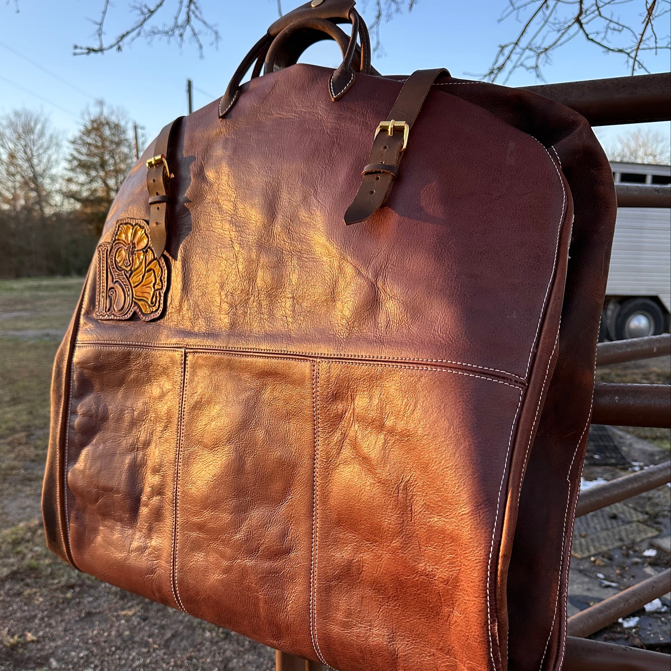 Brown leather garment bag with decorative emblem on a metal structure against a blue sky.